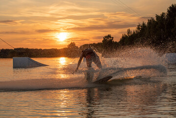 Wakeboarder making tricks. Low angle shot of man wakeboarding on a lake. Man water skiing at sunset.