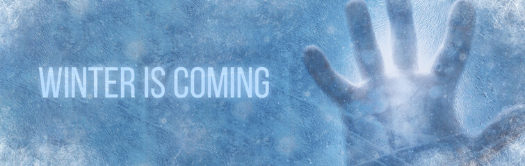 Banner of human hand against frozen glass with text winter is coming. Energy Crisis Concept.