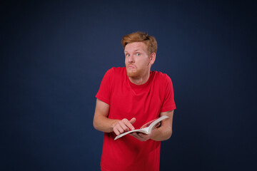 Young man study holding a book looking so confused and he does not understand anything, isolated on blue background