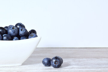 Blueberries in porcelain bowl and scattered on the table.