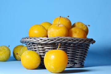 Fruit, yellow plum and in wicker basket. Blue background and copy space.