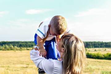 Mother and little son in the national Ukrainian dress. The mother holds the child in her arms against the background of a beautiful landscape in the summer