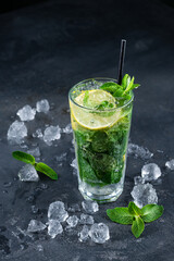 Fresh Mojito cocktail with lime, mint and ice in glass on dark background. Summer cold drink and cocktail