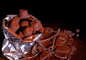 Lots of chocolate truffles in a packaging bag and slices of dark chocolate on a dark background. Selective focus