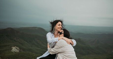 Young beautiful happy lesbian couple posing hugging in cloudy mountains outside at nature summer park. LGBT community concept. Female friends smiling enjoying moments together.