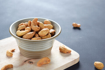 Roasted salted cashew nuts in ceramic bowl on natural wood and dark background.