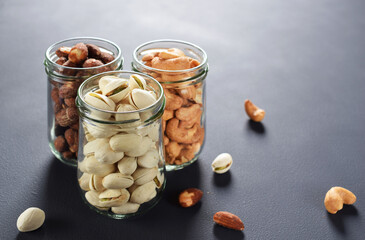 Healthy roasted nuts (cashew nut, almond, and pistachio) in glass bottles on dark background.