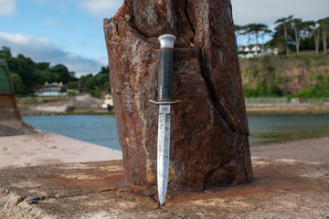 Commando dagger lens against a rusty post on the waterfront. Combat fighting knife used by special...
