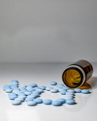 glass  bottle, with blue erection pills on white table with gray background
