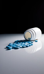 White plastic pill bottle with blue pills on white table. black background.  blue erection pills
