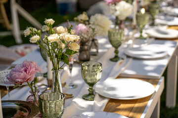 Fototapeta na wymiar Wooden table outdoors for a special occasion. Empty plates and unusual glasses. Vintage tray, candleholder and vases with beautiful flowers.