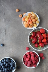 Many different ripe juicy berries in plates on the table. Summer flat lay. Raspberries, strawberries, cherries, cherries, blueberries.