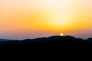 The hot sun hides behind the mountains on a summer day at dusk.