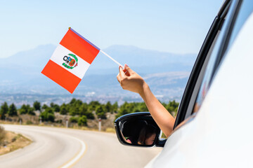 Woman holding Peru, flag from the open car window driving along the serpentine road in the mountains. Concept