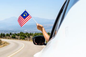 Woman holding Malaysia flag from the open car window driving along the serpentine road in the...