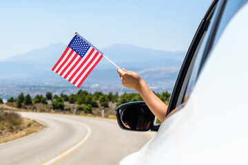 Woman holding USA flag from the open car window driving along the serpentine road in the mountains. Concept - 517346869