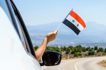 Woman holding Syria flag from the open car window driving along the serpentine road in the mountains. Concept