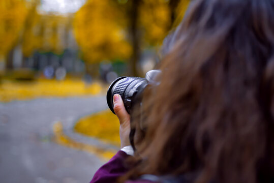 Young photographer woman with a camera taking a picture in the autumn park (face not shown)