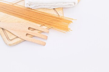spaghetti di Kamut da agricoltura biologica con tagliere in legno, forchettone e canovaccio in cotone bianco su sfondo bianco