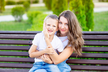 mom and her baby son in the park on a bench in the summer have fun hugging, laughing and playing