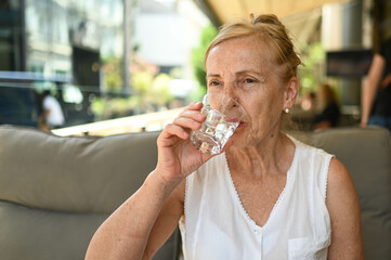 Happy senior woman perfect smile and teeth with glass of still water outdoors at summer sidewalk street cafe or restaurant terrace. Retired mature people holiday vacation, active lifestyle concept