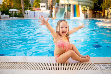 happy baby girl at the pool with water slides shouts hooray and laughs having fun on vacation,...