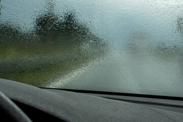 Driving the car on the highway during heavy rain. View from the front window toward the road. Windscreen full of blurry rain drops.