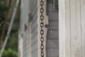 Rain chain and raindrops on the background of a Scandinavian style wooden house.