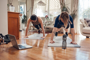 Fototapeta na wymiar Pretty women working out at home. Adult ladies with beautiful shaped bodies exercising in the apartment.