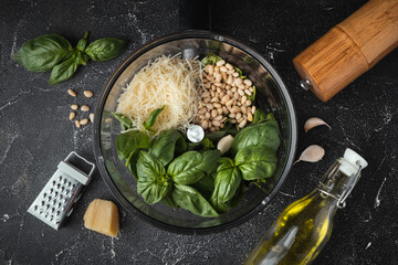 Ingredients for pesto sauce in the blender bowl. Green basil leaves, Parmesan cheese and pine nuts on the black background. Flat lay. Overhead view