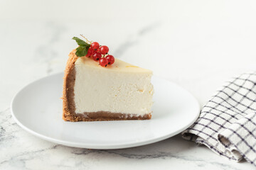 The piece of Classic New York cheesecake in the white plate decorated with red currant berries on the white background