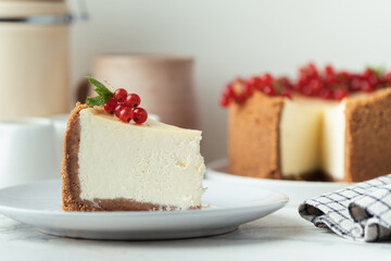 The piece of Classic New York cheesecake in the white plate decorated with red currant berries on the white background