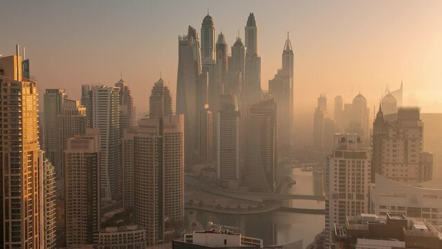 View of various skyscrapers in tallest recidential block in Dubai Marina during sunrise aerial timelapse with artificial canal. Many towers and yachts early foggy morning