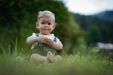 one year old blond german baby boy in bavarian dress with lederhose sitting outside on the meadow...