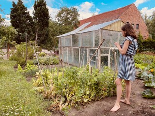 Mädchen steht vor einem Gewächshaus im Garten