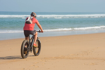Obraz na płótnie Canvas Mature man riding an electric fatbike on the beaches of Nouvelle-Aquitaine