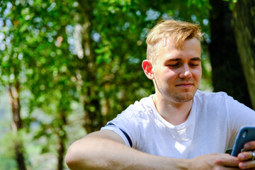 A young man in a white T-shirt communicates via SMS with a friend. Joyful emotions from...