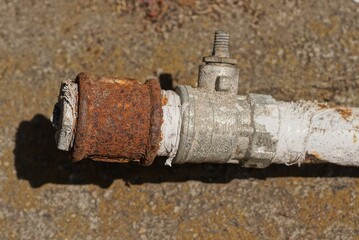 a piece of an old gray metal pipe with a broken faucet and a rusty brown nut on the ground