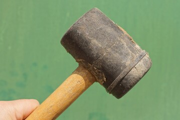 a hand holds a black plastic mallet hammer with a brown wooden handle on a green background