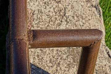 part of a brown iron rusty handrail from a metal pipe on a gray concrete in the street