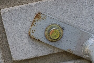 an iron bolt in a gray metal plate in a structure is screwed into a concrete wall