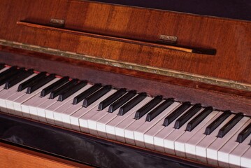 part of a brown old wooden piano with open white black keys in the room