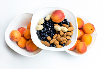A lot of fresh ripe apricots, almonds and blueberries that are very good for the eyes lie on the plates