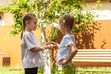 A six-year-old boy gives a girl a bouquet of flowers. Sunny day, in the garden the boy gives a bouquet of daisies to the girl.