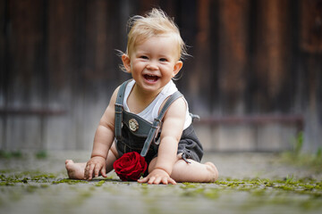 happy smiling one year old baby boy sitting or crawling in bavarian lether pants called Lederhosn...