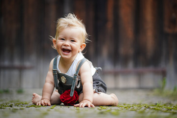 happy smiling one year old baby boy sitting or crawling in bavarian lether pants called Lederhosn...