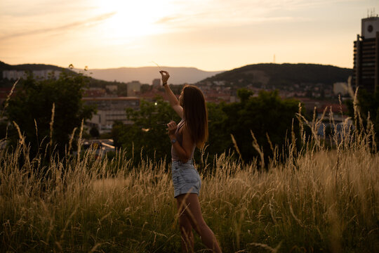 Young cheerful woman at sunset posing in the background of the city in the mountainsYoung woman looking at a flower through sunlight