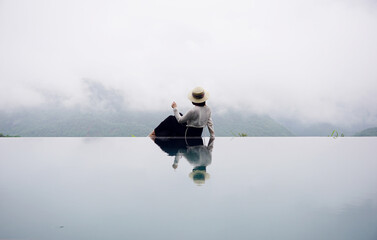 Woman sitting on the edge of a infinity pool on a cloudy day                               