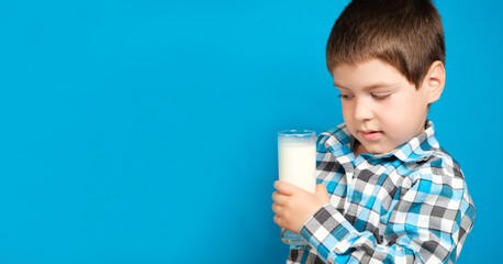 A beautiful boy of 4 years old holds a glass of milk and looks at it carefully, a banner with a...