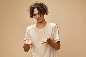 Unhappy discontented awesome tanned curly man in basic t-shirt with disgust looks aside posing isolated on beige background. Fashion New Collection offer. People Emotions concept. Free place for ad